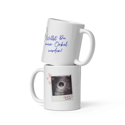 Zwei weiße Kaffeetassen übereinander gestapelt: Die obere zeigt den blauen Schriftzug „Willst Du mein Onkel werden?“, die untere ein Ultraschallbild im Polaroid-Stil mit der Aufschrift „Loading...“.