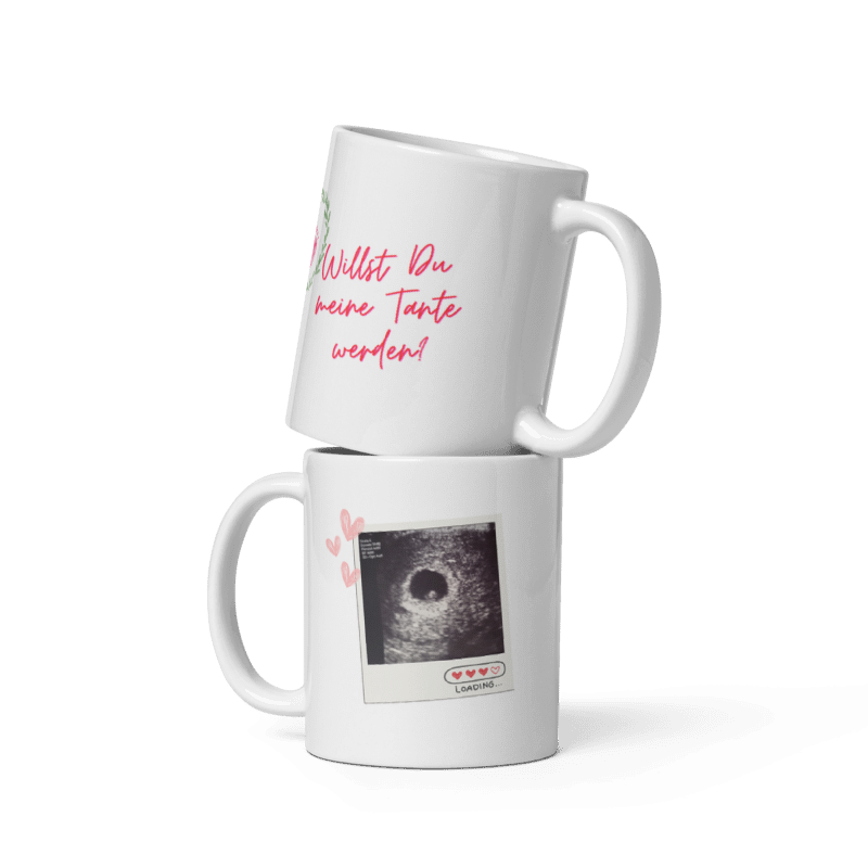 Zwei weiße Kaffeetassen übereinander gestapelt: Die obere zeigt den pinken Schriftzug „Willst Du meine Tante werden?“, die untere ein Ultraschallbild im Polaroid-Stil mit kleinen Herzen.