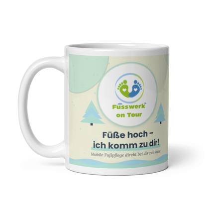Weiße Weihnachtstasse von Fusswerk on Tour, Vorderseite mit Logo der mobilen Fußpflege, kleinen Tannen und dem Spruch "Füße hoch – ich komm zu dir!"