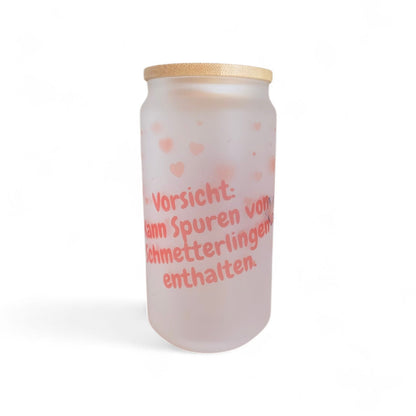 Seitliche Ansicht des mattierten Glases „Schmetterlingsmomente“, das den Schriftzug „Vorsicht: kann Spuren von Schmetterlingen enthalten“ und ein filigranes Schmetterlingsmotiv zeigt.