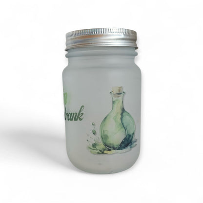 Detailaufnahme eines mattierten Trinkglases mit einer gruenen Zaubertrank-Flaschen-Illustration und einem angedeuteten Wasserspritzer-Design an der Seite.