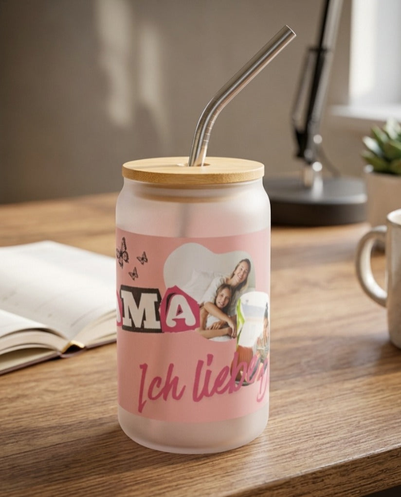 Ein mattiertes Glas mit Bambusdeckel und Metalltrinkhalm auf einem Holzschreibtisch. Das Glas ist mit einem personalisierten rosa Design „Mama ich liebe dich“, Fotos von Mutter und Kind sowie Schmetterlingen bedruckt. Im Hintergrund sind ein Buch und eine Schreibtischlampe in einer gemütlichen, hellen Atmosphäre zu sehen.