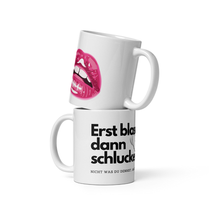 Eine rechte Hand hält eine weiße Kaffeetasse mit Henkel rechts. Auf der Tasse ist ein pinkes Lippen-Motiv und teilweise der Spruch „Erst blasen, dann...“ zu sehen.