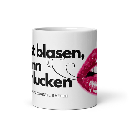 Schräge Vorderansicht einer weißen Kaffeetasse mit schwarzem Spruch, Windhauch-Grafik und einem pinken Lippen-Motiv auf schwarzem Hintergrund.