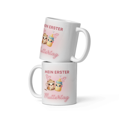 Zwei gestapelte weiße Tassen von Schlucksachen mit dem Aufdruck Mein erster Muttertag, illustriert mit einer niedlichen Kaffeetasse, einem Babyfläschchen und rosa Herzen.