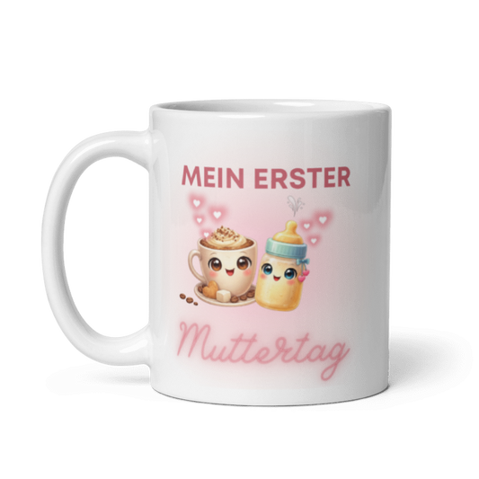 Weiße Keramiktasse mit dem Motiv Mein erster Muttertag, abgebildet mit einer Kaffeetasse, einem Babyfläschchen und kleinen Herzen, Henkel auf der linken Seite.